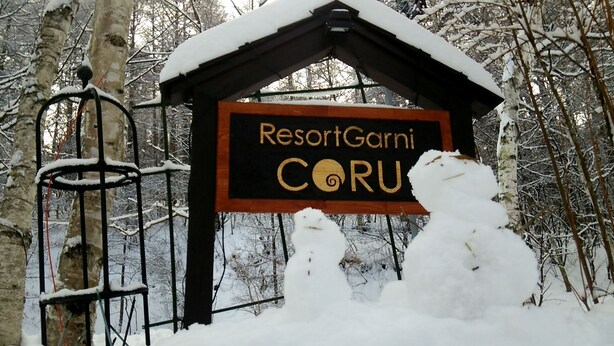 Señal de ResortGarni CORU con un techo cubierto de nieve y una valla metálica en primer plano.