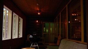 Interior acogedor de una cabaña con techo de madera, un sofá blanco, una parrilla y ventanas amplias.