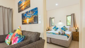 A bedroom with a bed, a sofa, and two wall-mounted paintings. - Cook Islands Holiday Villas Turangi (Rarotonga)