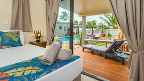 A hotel room with a bed, a view of the pool, and a lounge area with chairs and a table. - Cook Islands Holiday Villas Turangi (Rarotonga)