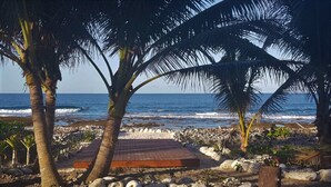 A beach with palm trees, a wooden deck, and a rocky shoreline. - Cook Islands Holiday Villas Turangi (Rarotonga)
