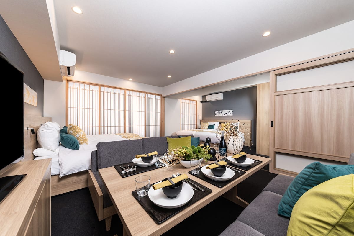 A modern hotel room with a dining area, a bed with a view, and a small kitchenette.