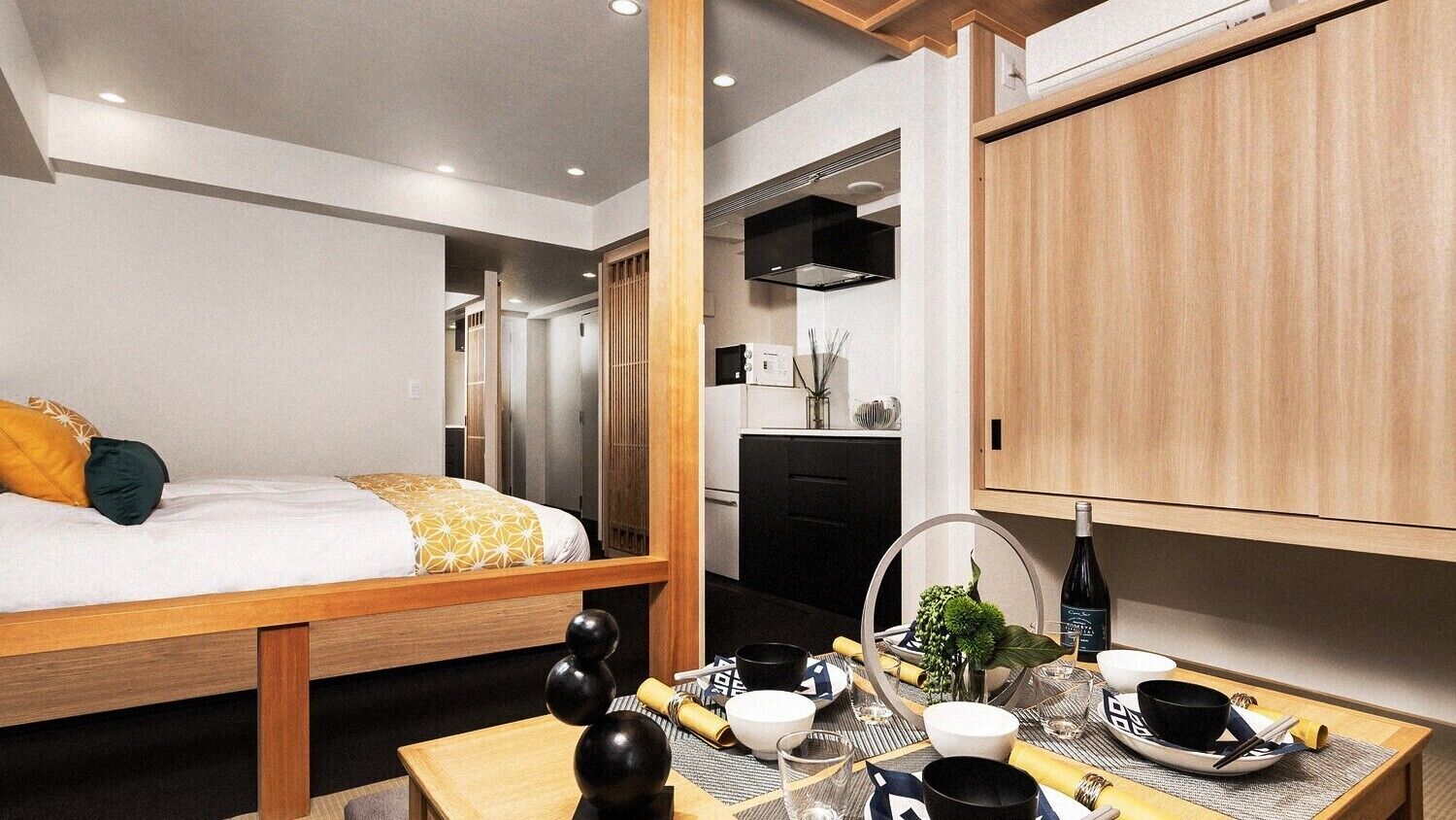 Una habitación de hotel compacta con una cama, una pequeña mesa de comedor, una kitchenette y un armario de madera.