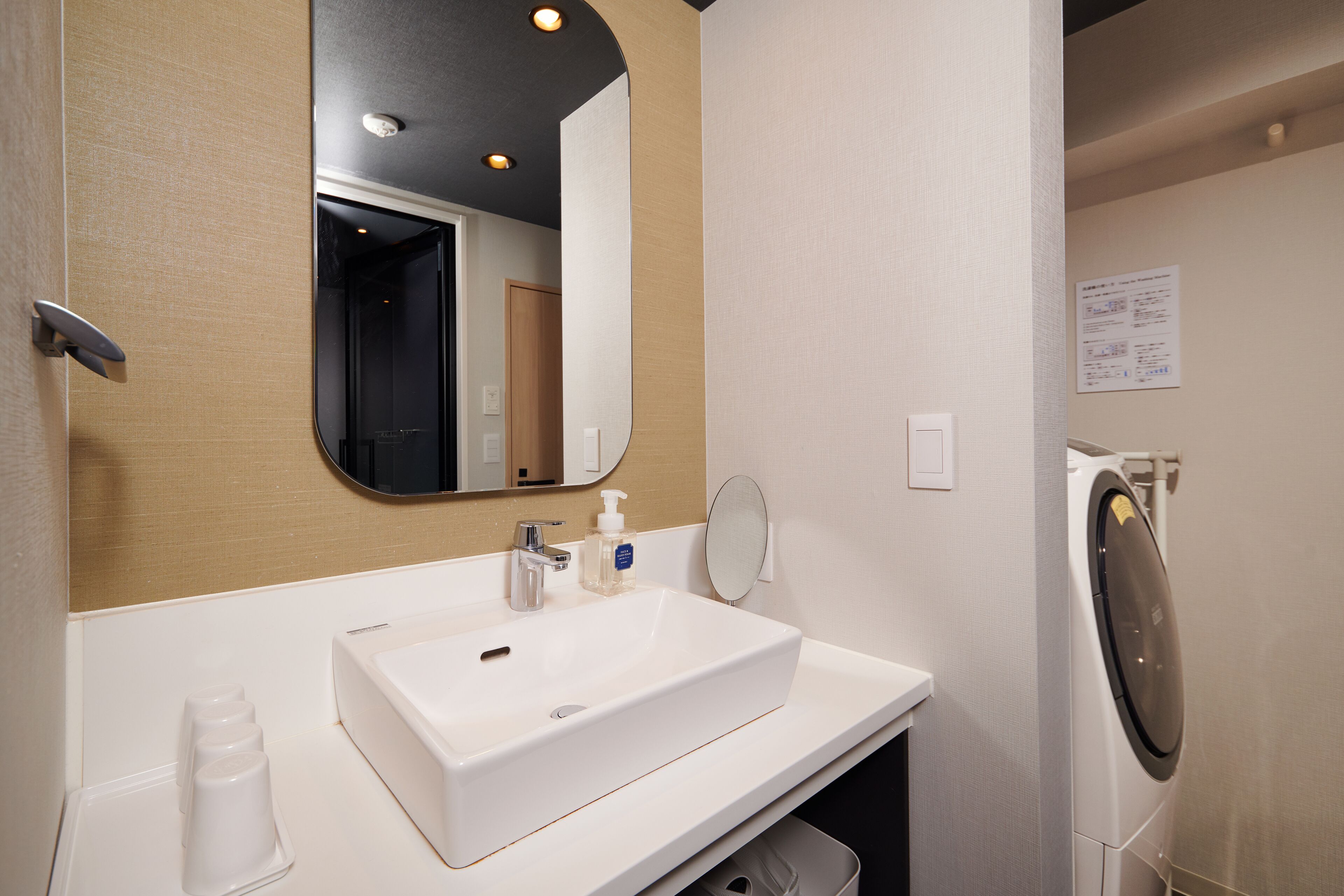 A hotel bathroom with a white sink, mirror, and a washing machine.