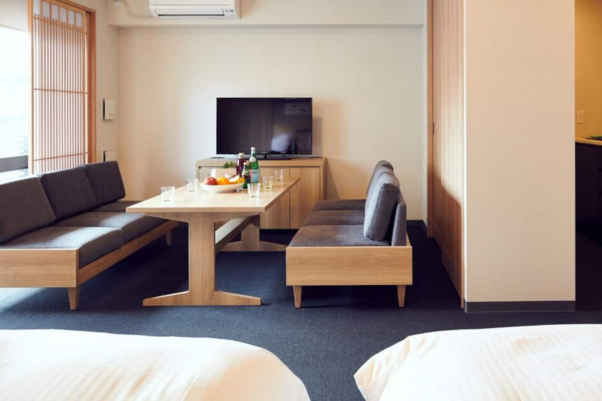 A hotel room with a sofa, a dining table with a fruit bowl, a television, and a kitchenette.
