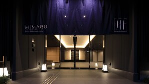 La entrada del Mimaru Apartment Hotel, con un diseño moderno, presenta una fachada oscura, una entrada iluminada y un letrero claro.