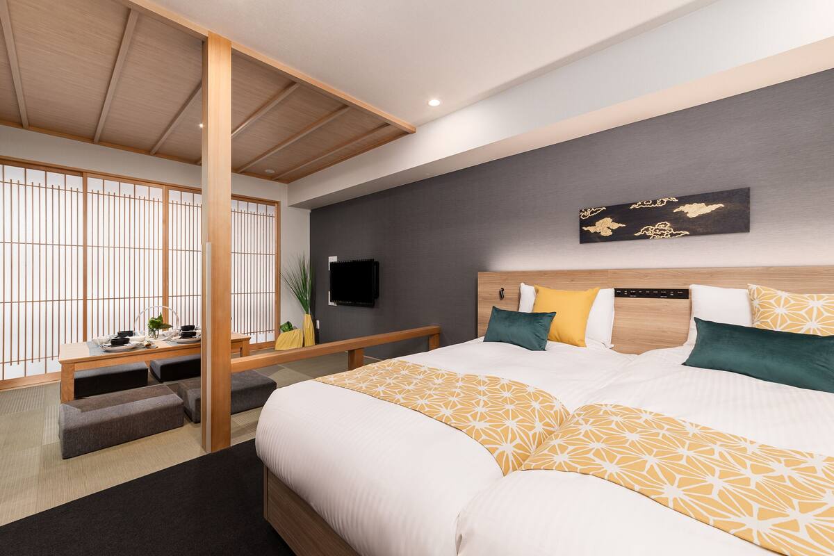 A modern hotel room with a large bed, a TV mounted on the wall, and a traditional Japanese sliding door.