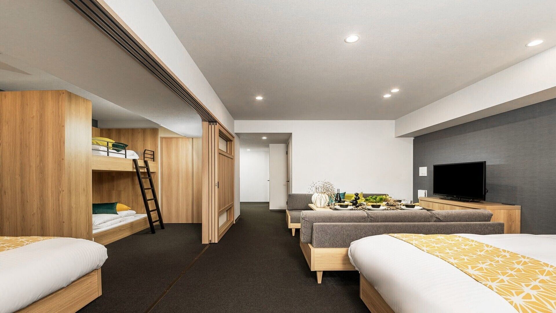A modern hotel room with bunk beds, a desk, a flat-screen TV, and a dining area.