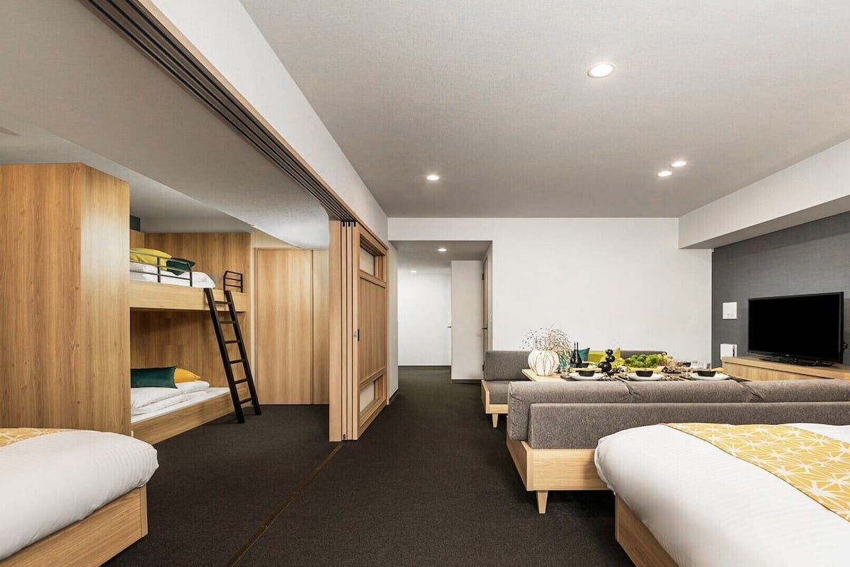 A modern hotel room with bunk beds, a desk, a flat-screen TV, and a dining area.