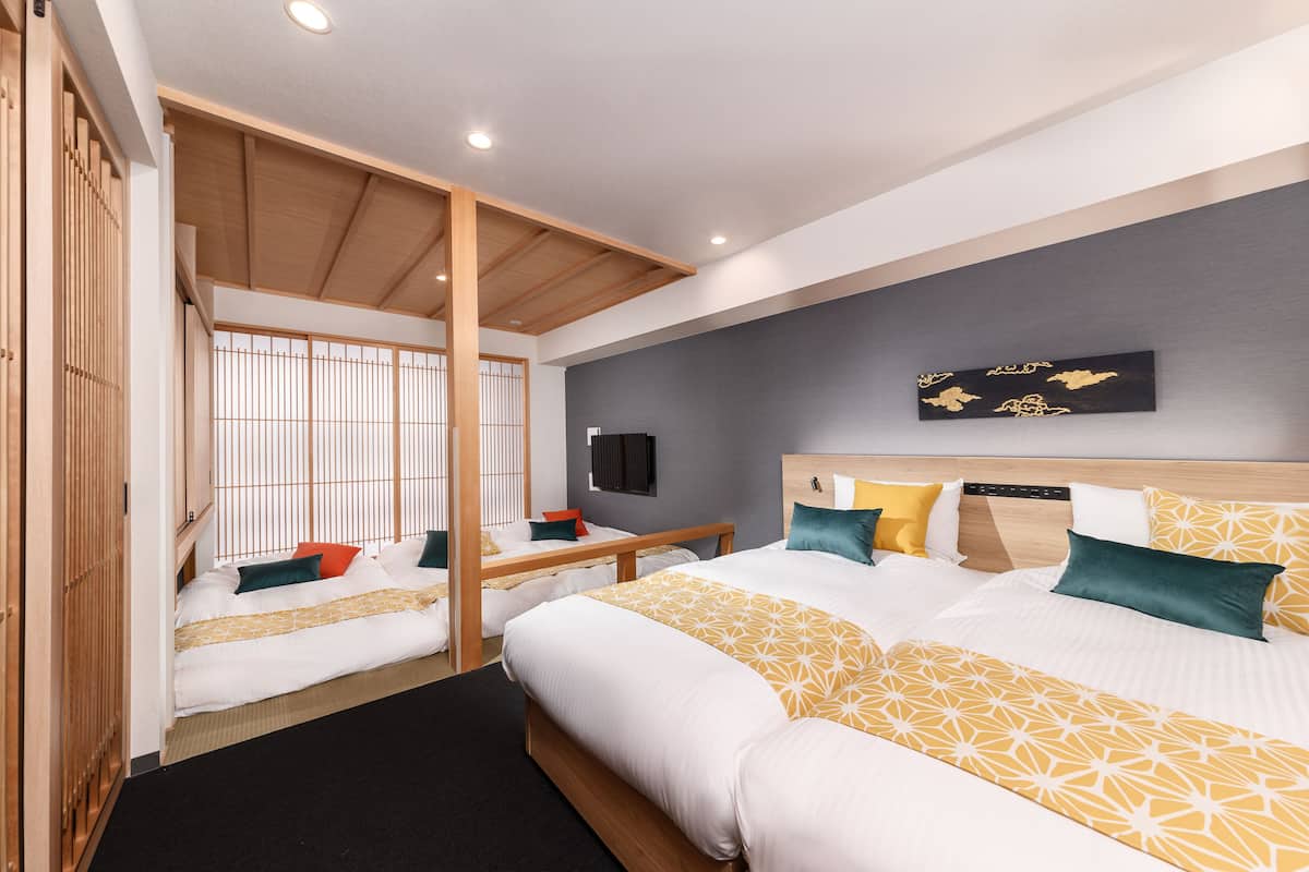 A hotel room with two beds, a wooden ceiling, a black wall with a gold artwork, and a black TV.