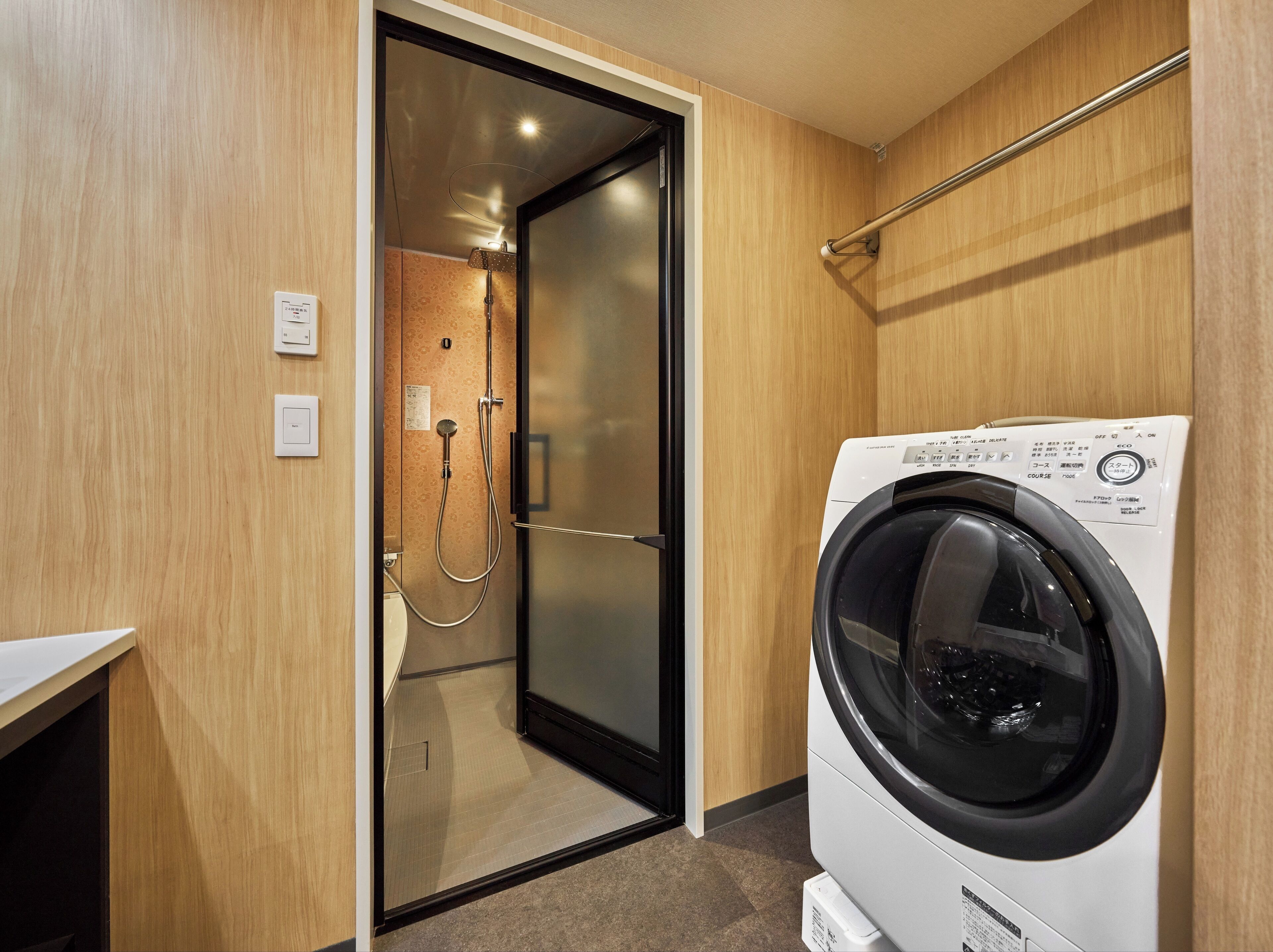 Ett kompakt hotellrum med tvättmaskin, en duschhörna och en väggpanel i trä.
