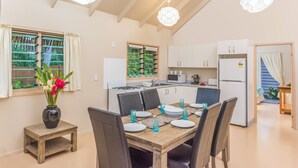A modern kitchen with white cabinets, a dining table set for four, and a vase with flowers on a side table. - Cook Islands Holiday Villas Muri (Rarotonga)
