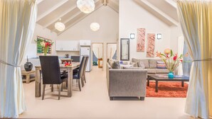 A spacious living area with a dining table, chairs, a sofa, and a coffee table. There are decorative wall art pieces and a vase with flowers. - Cook Islands Holiday Villas Muri (Rarotonga)