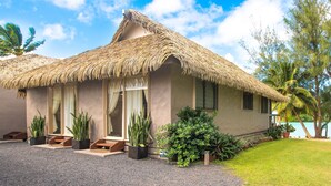 A thatched-roof bungalow with a gravel driveway, potted plants, and a view of the ocean. - Cook Islands Holiday Villas Muri (Rarotonga)