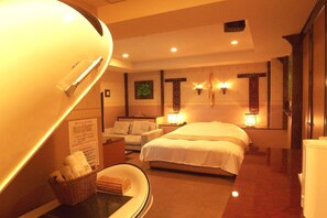 A hotel room with a bed, a desk with a lamp, a chair, a small table with a basket, and a wall-mounted shelf. - HOTEL Sweets (Yawata)