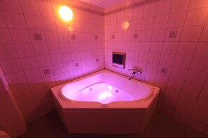 A bathroom with a large, rectangular bathtub, a small wall-mounted television, and a light fixture above the tub. - HOTEL Sweets (Yawata)