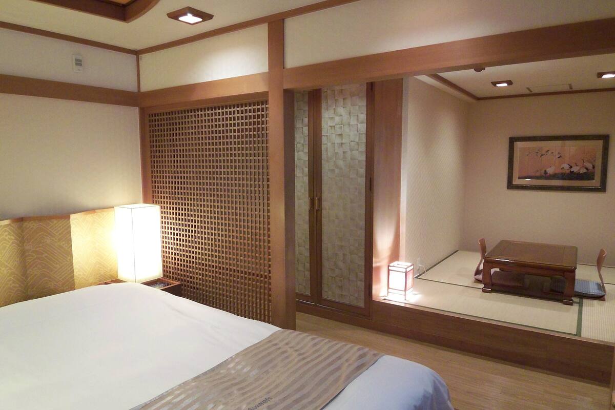 A hotel room with a bed, a nightstand, a wooden desk, and a sliding door.