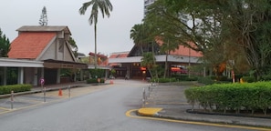 A hotel entrance with a covered walkway, palm trees, and a parking area. - ETM Awana Homestay (Genting Highlands)