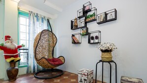 A room with a wicker chair, a decorative vase, and a wall-mounted shelf with various items. - Little Pig Home - Hostel (Da Nang)