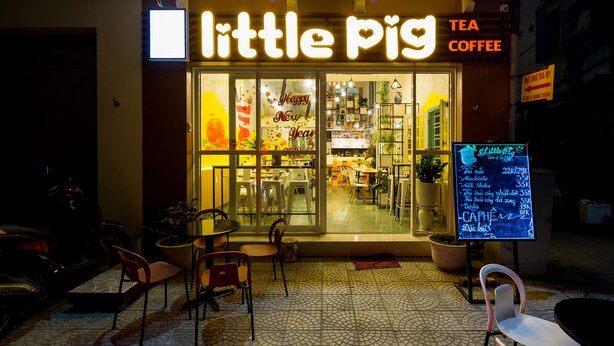 A cozy cafe named "Little Pig Tea Coffee" with a bright sign, outdoor seating, and a menu board outside. - Little Pig Home - Hostel (Da Nang)