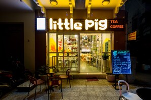 A cozy cafe named "Little Pig Tea Coffee" with a bright sign, outdoor seating, and a menu board outside. - Little Pig Home - Hostel (Da Nang)