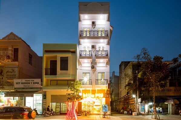 A multi-story building with a brightly lit ground floor featuring a cafe named "Little Pig Tea Coffee".