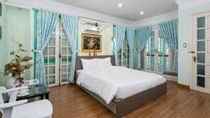 A bedroom with a bed, a glass table, and a chair. There is a window with curtains, a picture on the wall, and a door. - Little Pig Home - Hostel (Da Nang)