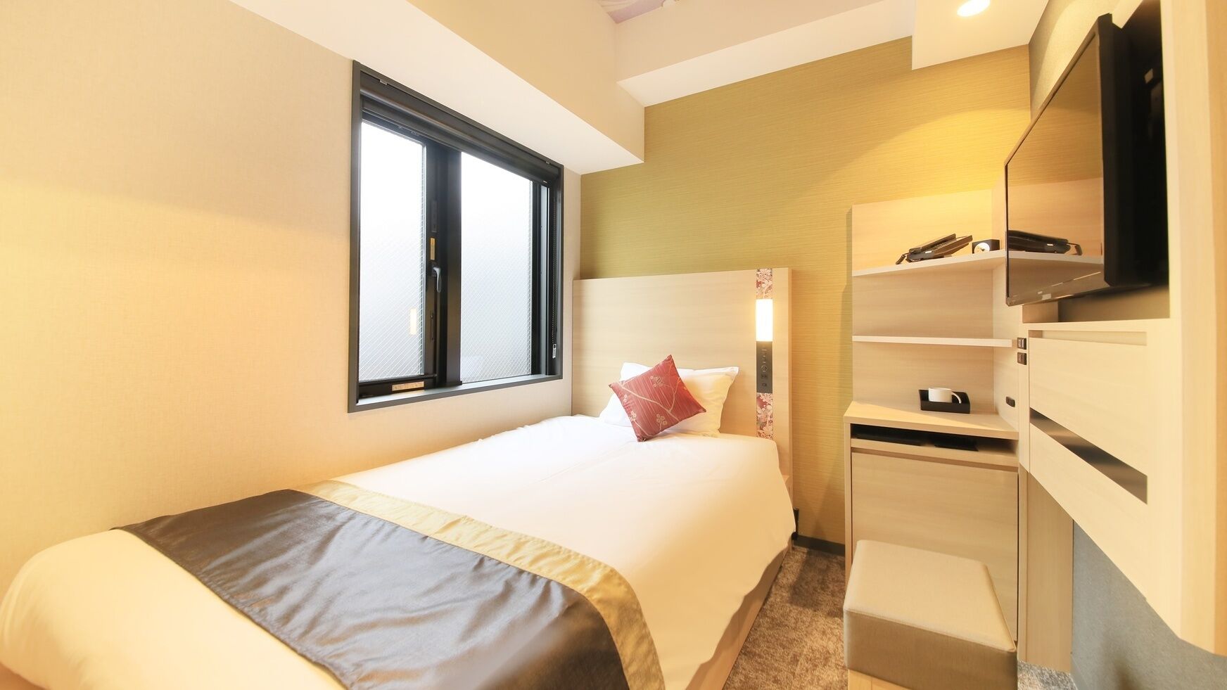 A hotel room with a bed, a desk, a TV, and a window.