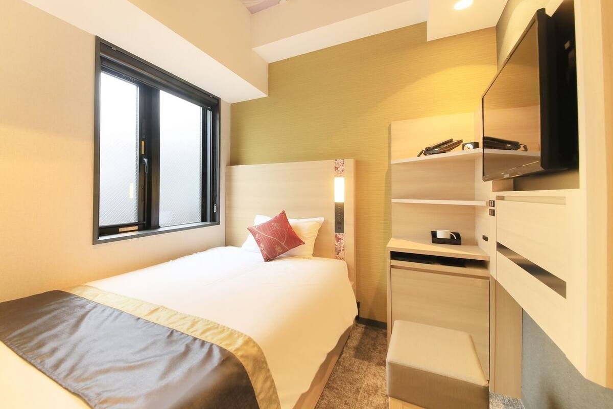 A hotel room with a bed, a desk, a TV, and a window.