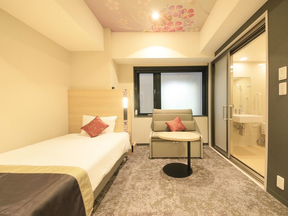 A hotel room with a bed, a sofa, a small table, and a glass shower area.