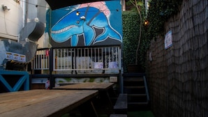 An outdoor seating area with wooden tables and benches, a mural of a blue creature on the wall, and a bamboo fence. - Hump Backpackers (Potts Point)