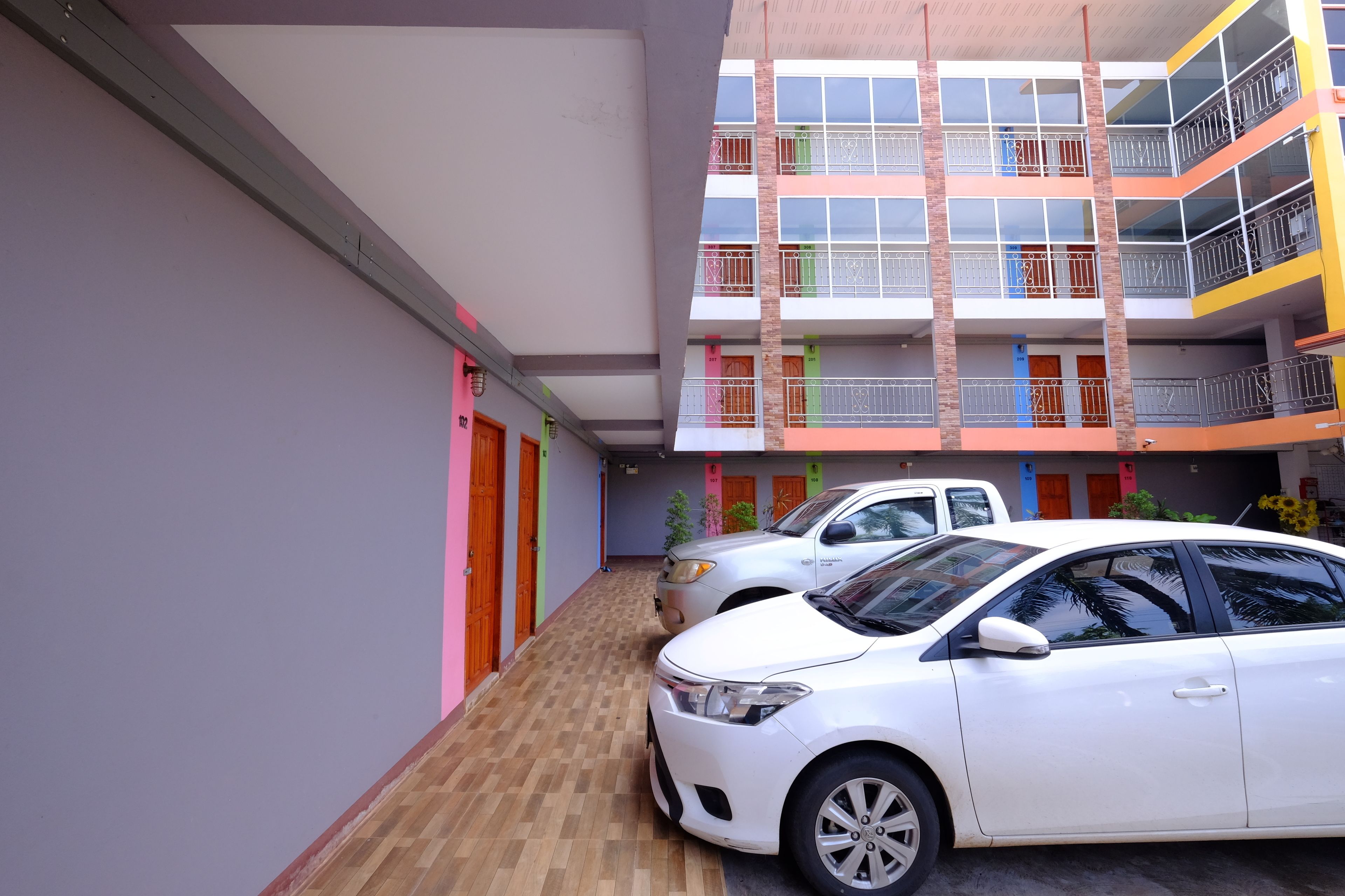 A multi-story building with balconies, a car parked in front, and a wooden floor.