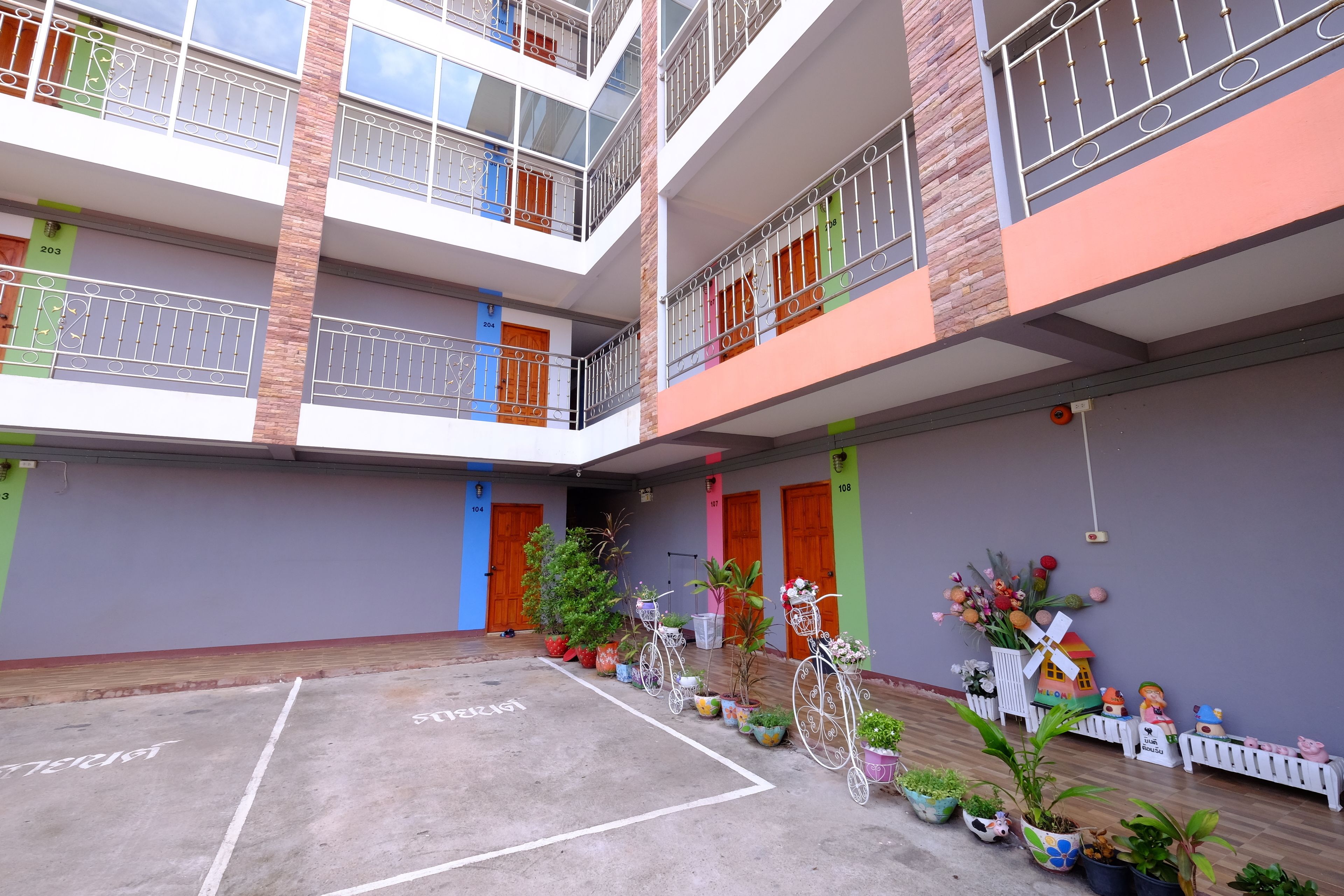 Un edificio de varios pisos con balcones, un patio con plantas en macetas y un aparcamiento para bicicletas.