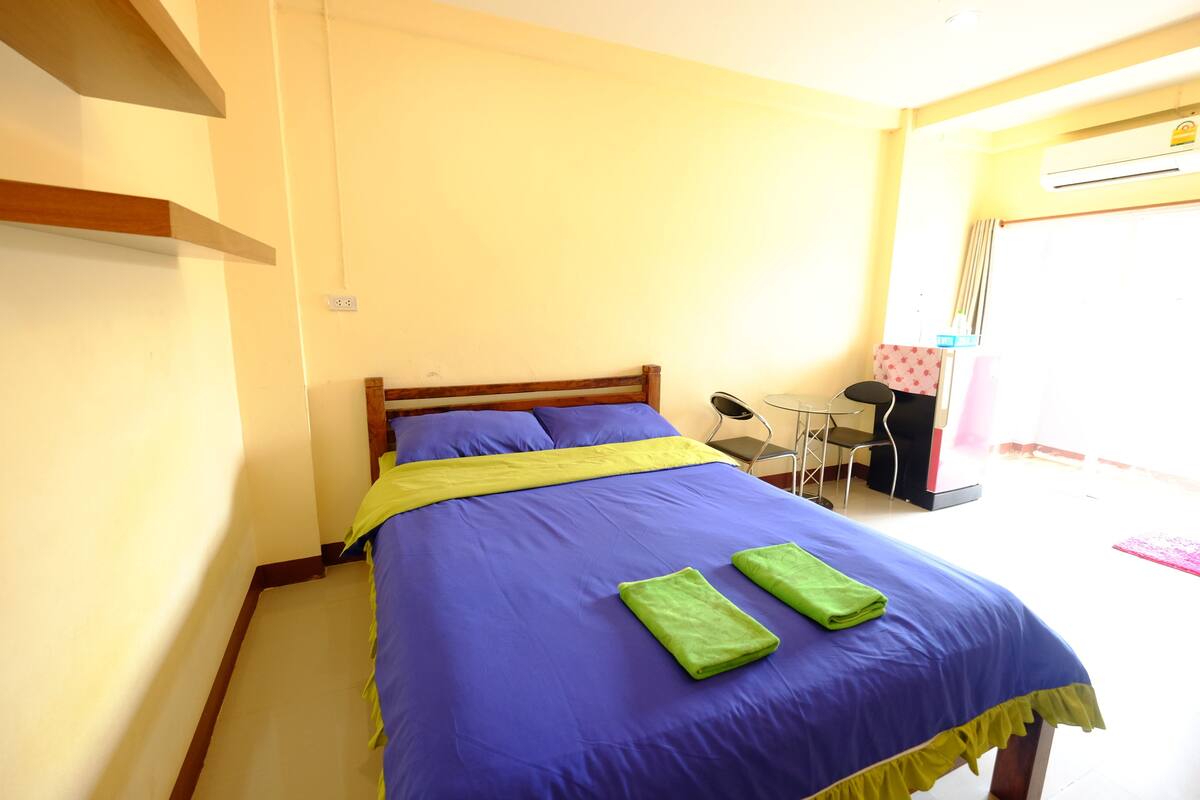 A neatly made bed with a blue and yellow bedspread, two green towels, and a wooden headboard.