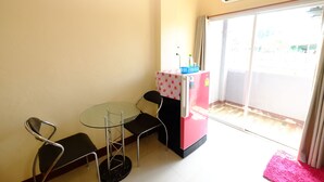 Une petite pièce avec une table en verre et deux chaises, un réfrigérateur rose et une porte-fenêtre coulissante donnant sur l’extérieur.