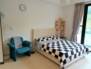 A bedroom with a bed, a chair, a bedside table, a clock, a shelf with stuffed toys, and a window with curtains. - ETM Midhill Family Studio (Genting Highlands)