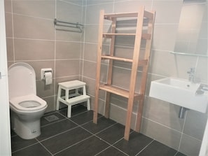 A bathroom with a toilet, a small white step stool, a wooden shelf unit, and a sink. - ETM Midhill Family Studio (Genting Highlands)