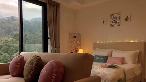 A bedroom with a bed, a sofa, and a view of a forest through a large window. - ETM Midhill Genting Scenery Studio Room (Genting Highlands)