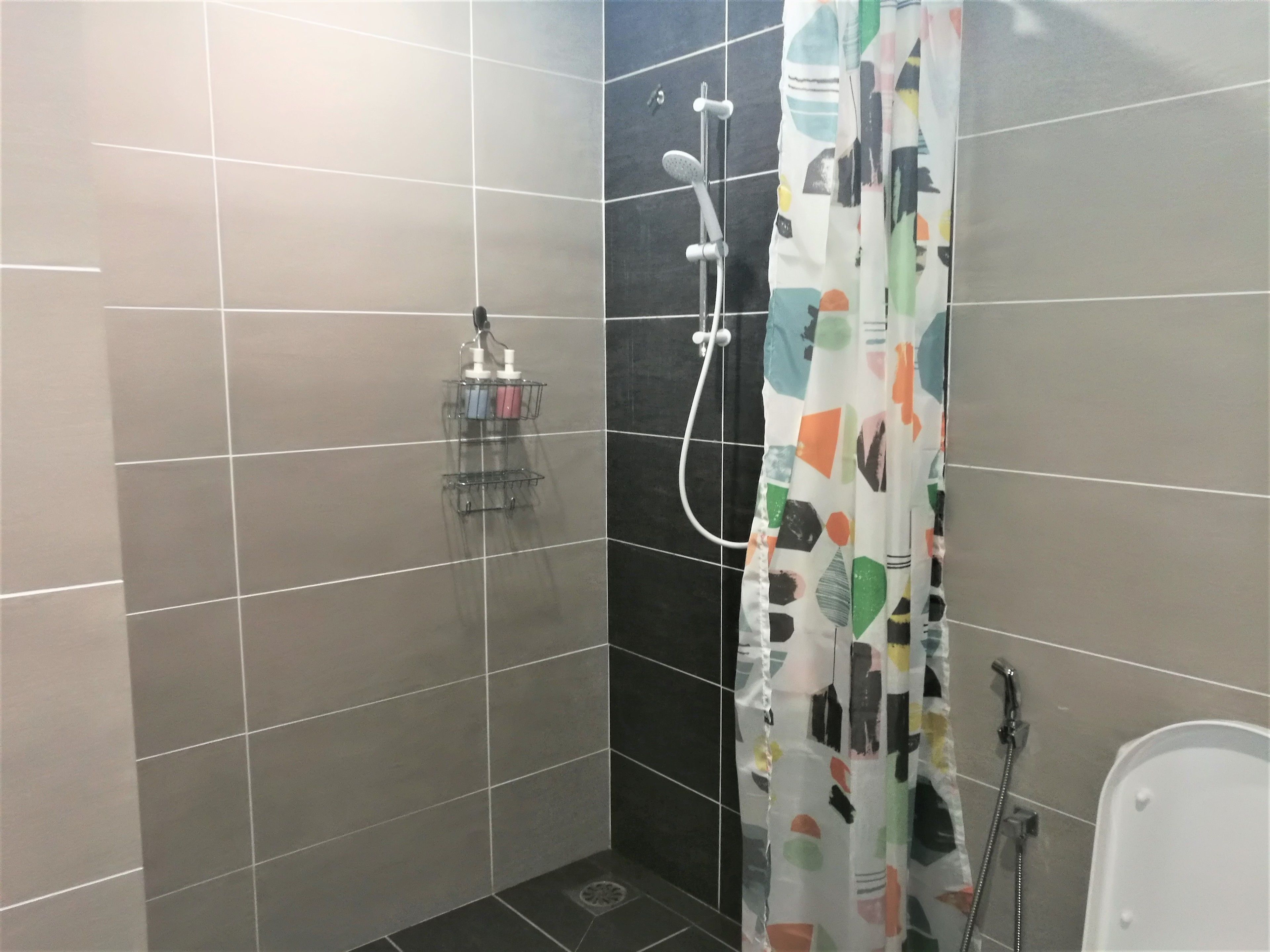 A small, tiled shower area with a shower curtain, a handheld showerhead, and a wall-mounted faucet.
