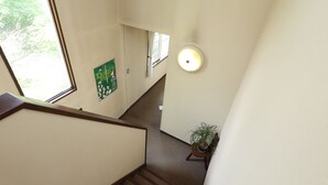 A staircase with a wooden handrail, a potted plant, and a wall-mounted light fixture. - Melange (Fujikawaguchiko)