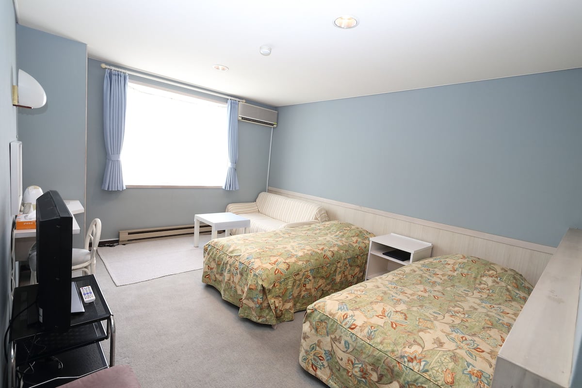 A bedroom with two beds, a desk, a chair, and a window with curtains.