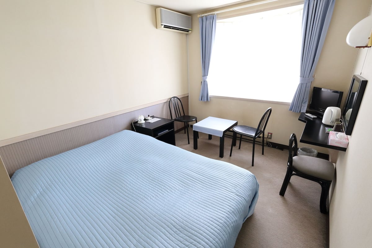 A hotel room with a bed, a desk, a chair, a television, and a window with curtains.