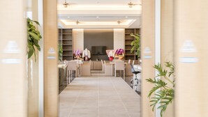 A modern hotel lobby with a central seating area, a flat-screen TV, and potted plants. - Lieta Nakayama (Nago)