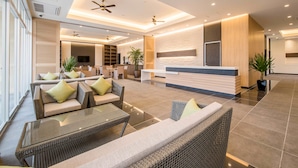A spacious lobby with wicker furniture, a reception desk, and ceiling fans. - Lieta Nakayama (Nago)