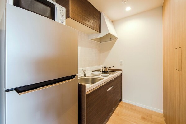 Una cocina compacta con un refrigerador blanco, gabinetes de madera oscura, un lavamanos de acero inoxidable y una encimera de color claro.