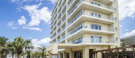 Un hôtel à plusieurs étages doté de balcons, d’une entrée couverte et de palmiers au premier plan.