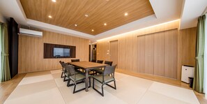 A modern room with a wooden ceiling, a flat-screen TV mounted on the wall, a dining table with chairs, and a wardrobe. - Lieta Nakayama (Nago)