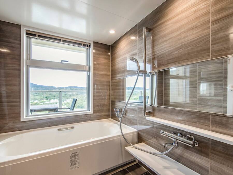 A modern bathroom with a bathtub, a large mirror, and a window with a view.