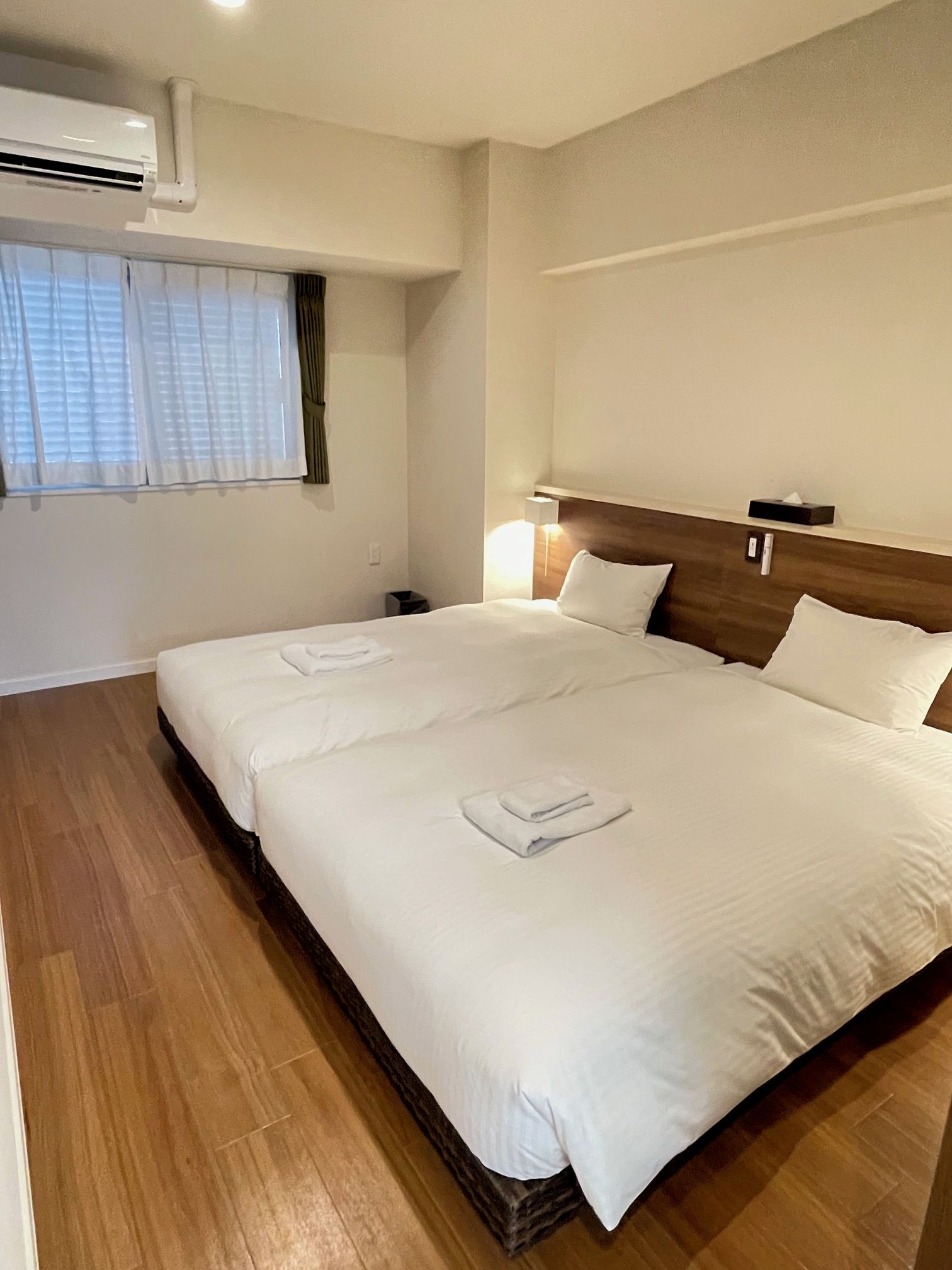 A hotel room with a large bed, a nightstand, a lamp, and an air conditioning unit.