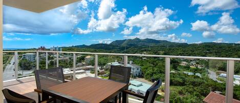 A balcony with a wooden table and chairs, offering a view of a cityscape and mountains.